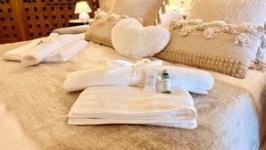 Een net opgemaakt bed met opgevouwen handdoeken, een hartvormig kussen en een flesje lotion.
