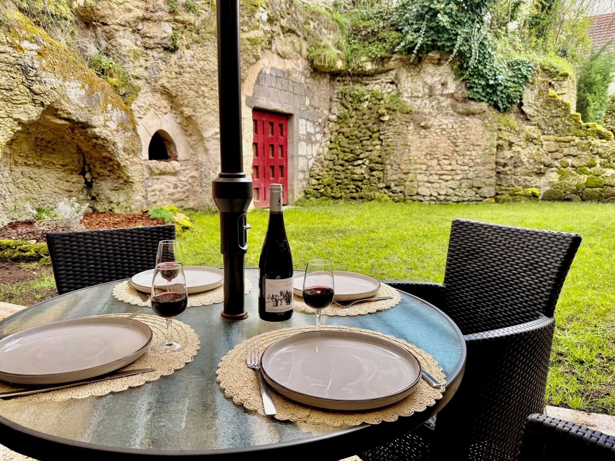 Ein Essplatz im Freien mit Tellern, Gläsern und einer Flasche, vor einer Steinwand und Grünpflanzen.
