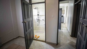 A hallway leading to a shower area with a tiled floor and a pair of slippers. - Vo Homes, Modern Kisasi, Kulambiro kyanja Retreat  Quiet, Secure, WiFi Near City (KAMPALA)