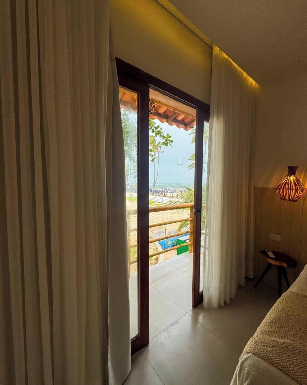 A room with a view of a beach, a sliding door, a bed, and a lamp.