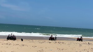 Ein Strand mit vier Quad-ATVs, die im Sand geparkt sind, einem klaren Himmel und dem Meer im Hintergrund.