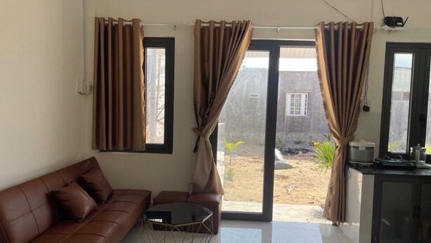 Ein Wohnzimmer mit braunem Ledersofa, einem Glastisch und Blick auf einen Innenhof mit Pflanzen und einem Gebäude.