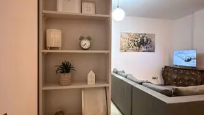 Ein Wohnzimmer mit einer Couch, einem Fernseher, einem Bücherregal mit Dekoration und einem Gemälde an der Wand.