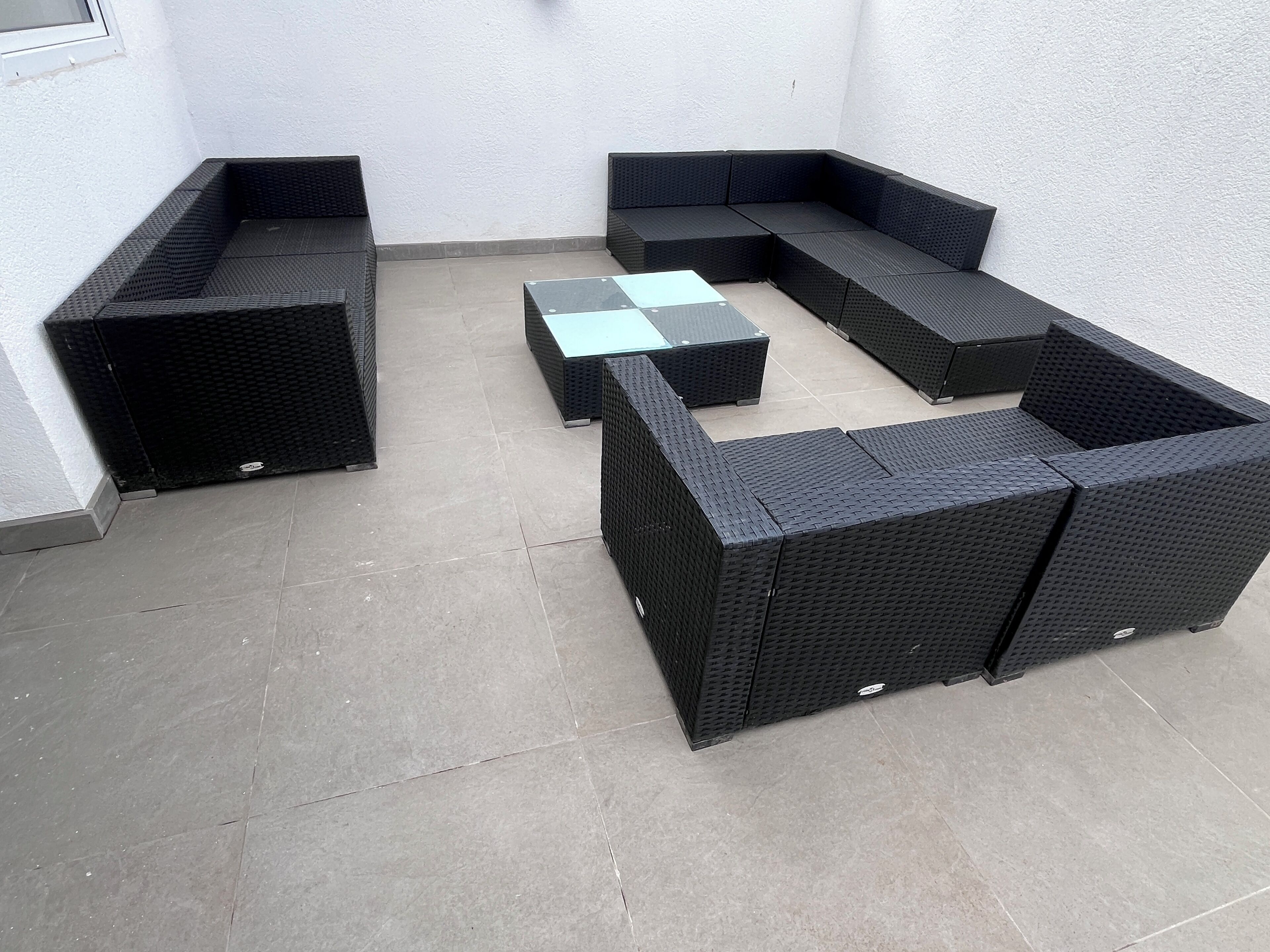 Ein winkelförmiger Patio-Bereich mit schwarzer Rattanmöbeln, darunter eine Couch und zwei quadratische Tische.