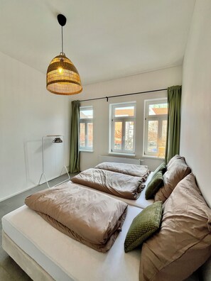 A bedroom with a bed, a hanging light fixture, and windows with curtains. - Old town apartment • central - quiet - Terrace - Parking lot - (Erfurt)