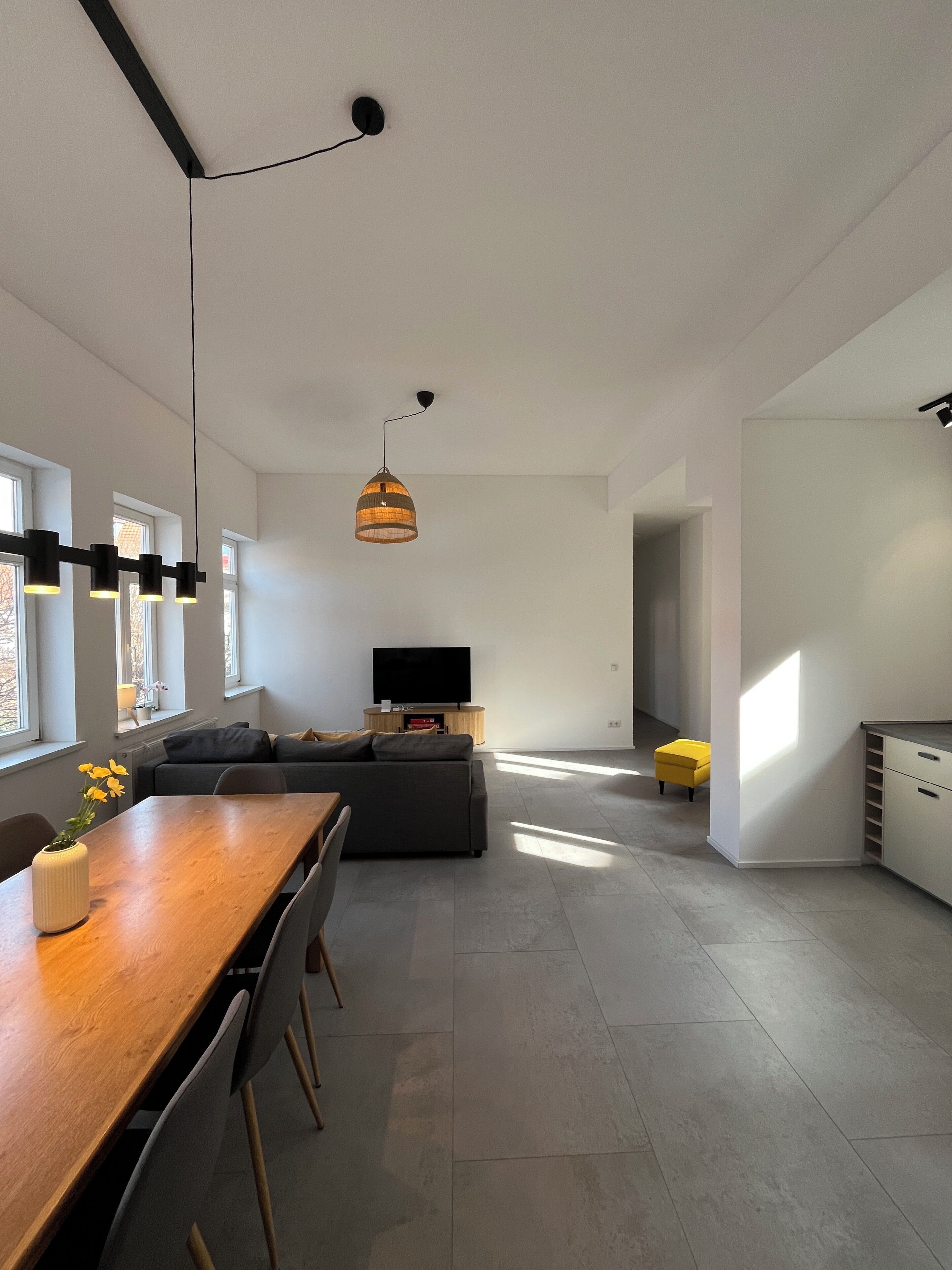 A modern living space with a dining area, sofa, TV, and a bright corner with a yellow chair.