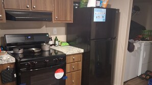 Una cocina con armarios de madera, estufa negra, refrigerador y encimera.
