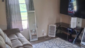 Una sala de estar con sofá, televisor, ventilador y ventana con cortinas.