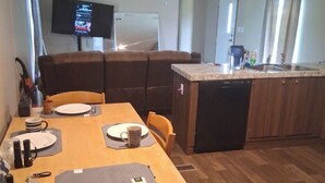 Una cocina compacta con comedor, un televisor montado en la pared y piso de madera.