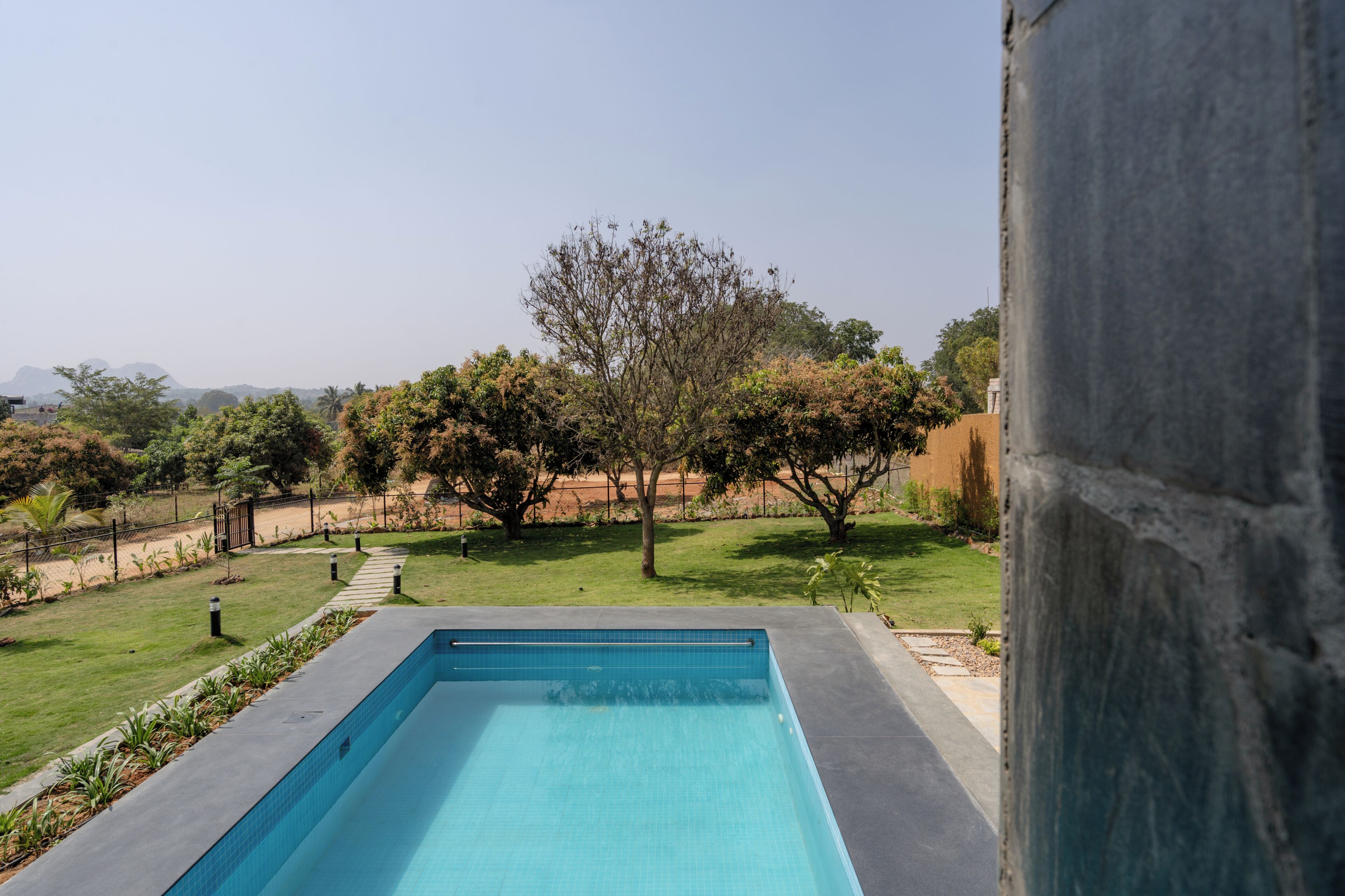 A rectangular swimming pool with a clear blue water surface, surrounded by a well-maintained lawn and trees.
