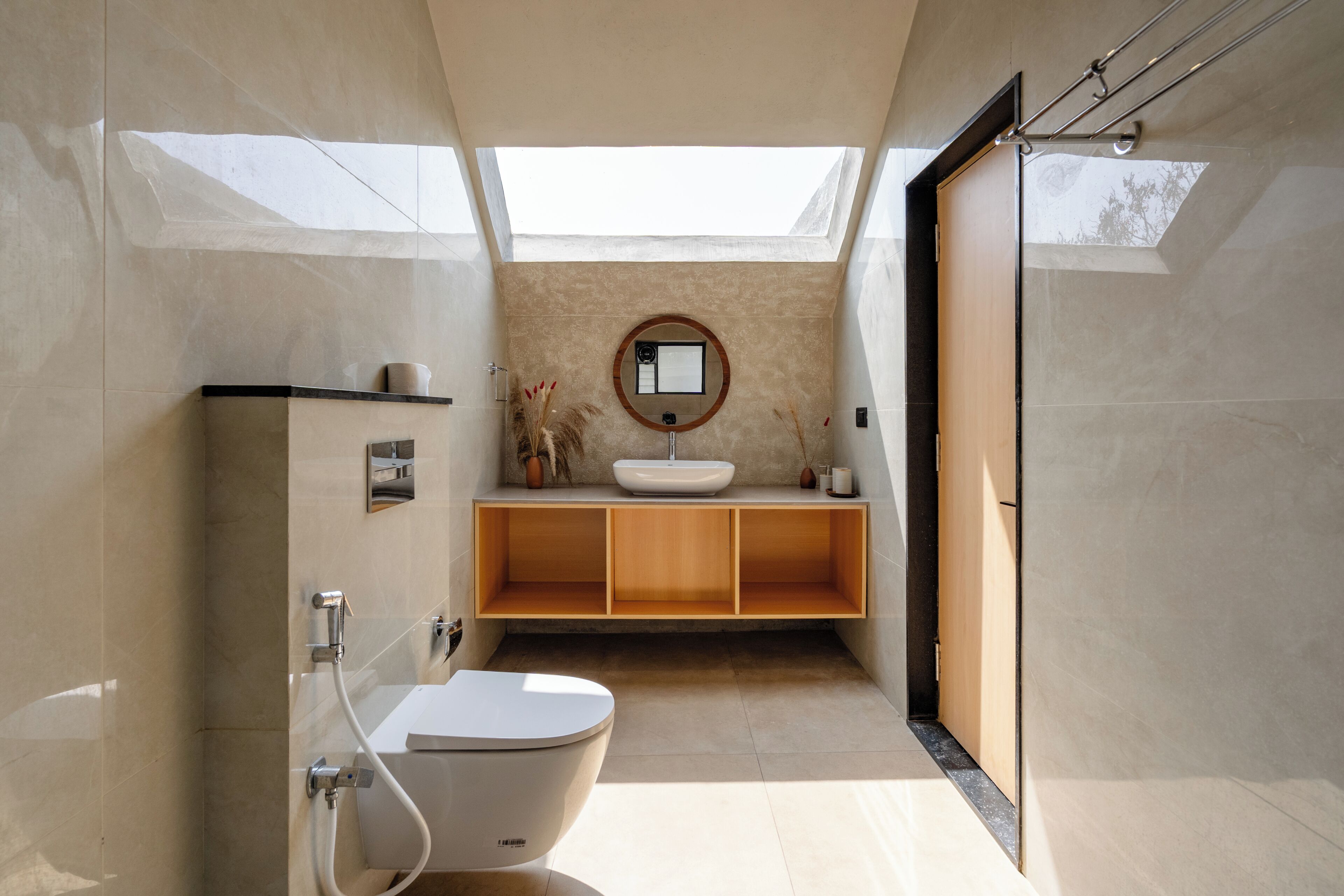 Et moderne badeværelse med ovenlys, et fritstående toilet, et håndvaskarrangement og et spejl.
