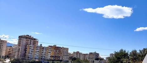 A balcony with a metal railing, a clear blue sky, and residential buildings in the background.