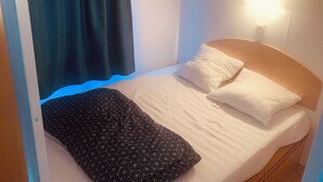 Une petite chambre à coucher avec un lit simple, une couverture à motifs, un oreiller blanc et un rideau noir.