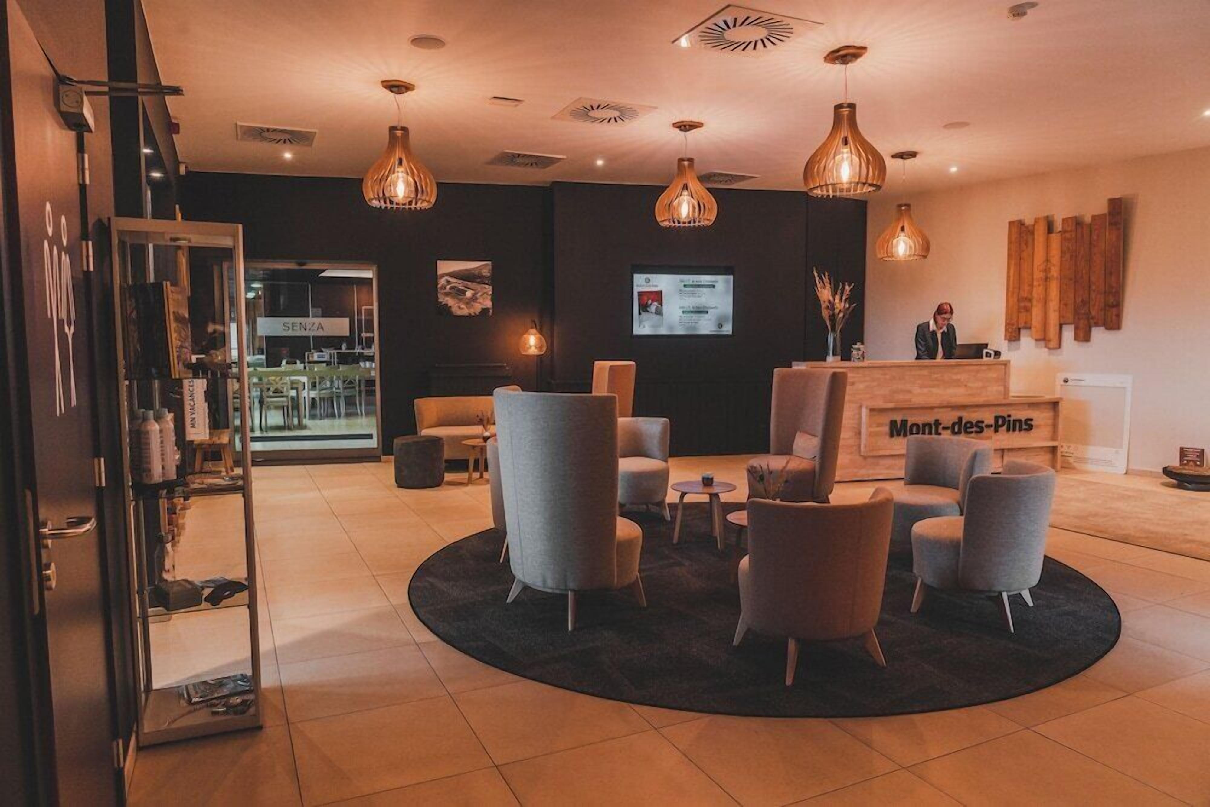 Een moderne hotel lobby met een receptiebalie, een zithoek en een groot scherm met informatie.