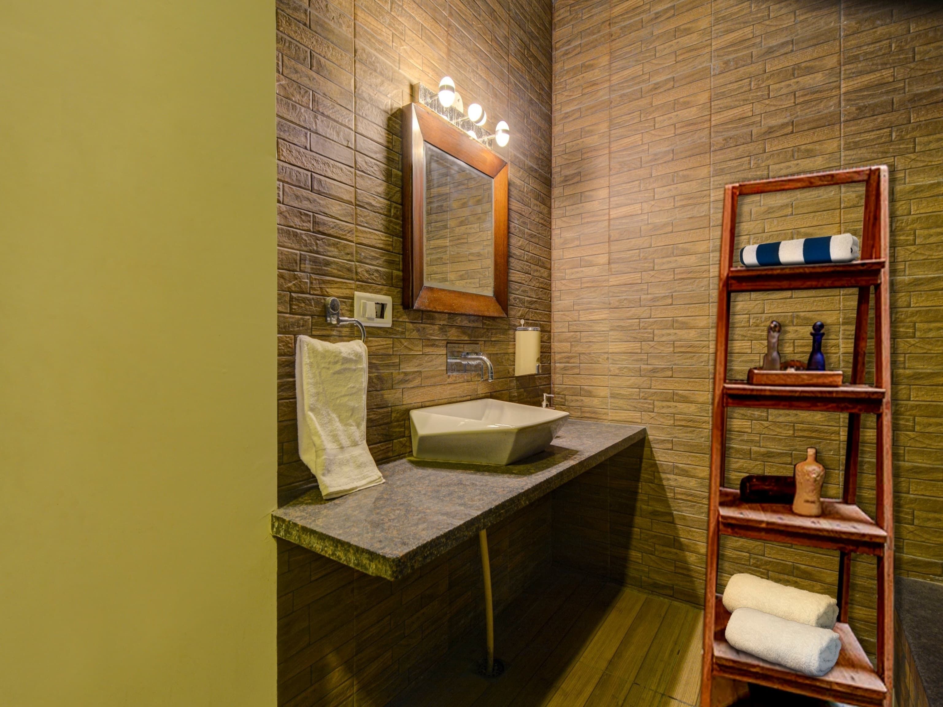 Une salle de bain avec un lavabo en pierre, un miroir, un porte-serviettes et une étagère contenant des articles de toilette.