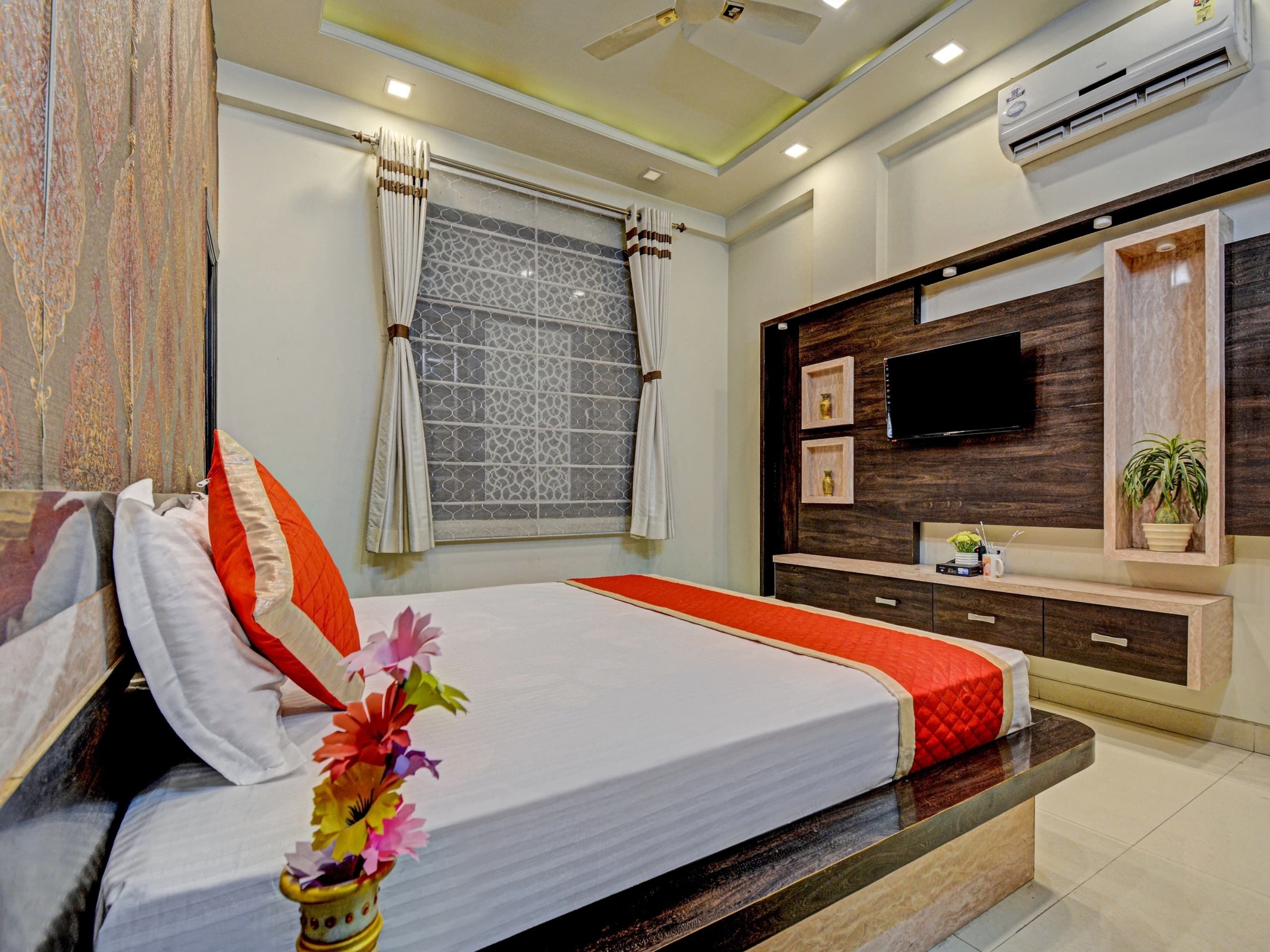 Un dormitorio con cama, cortinas, televisor y estante de pared para televisión.