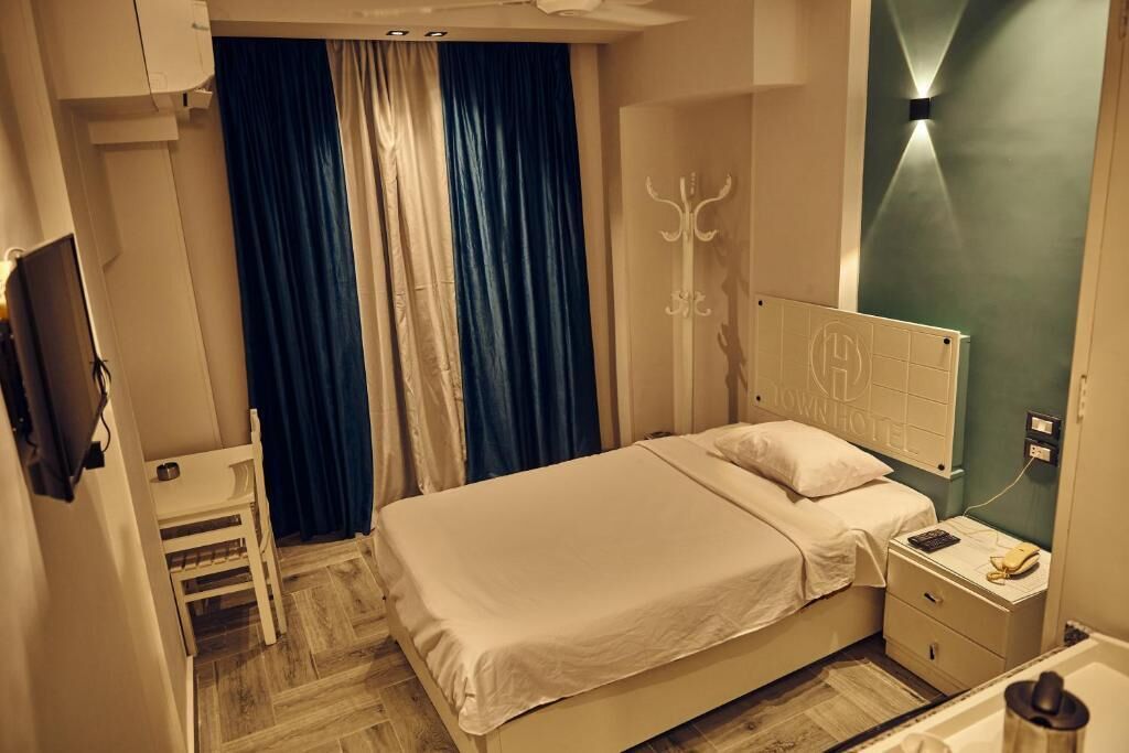 A hotel room with a bed, bedside table, chair, and a TV mounted on the wall.