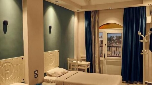 A hotel room with two beds, a small table, a chair, a coat rack, and a view of the outside. - Town Hotel Hurghada (Hurghada)