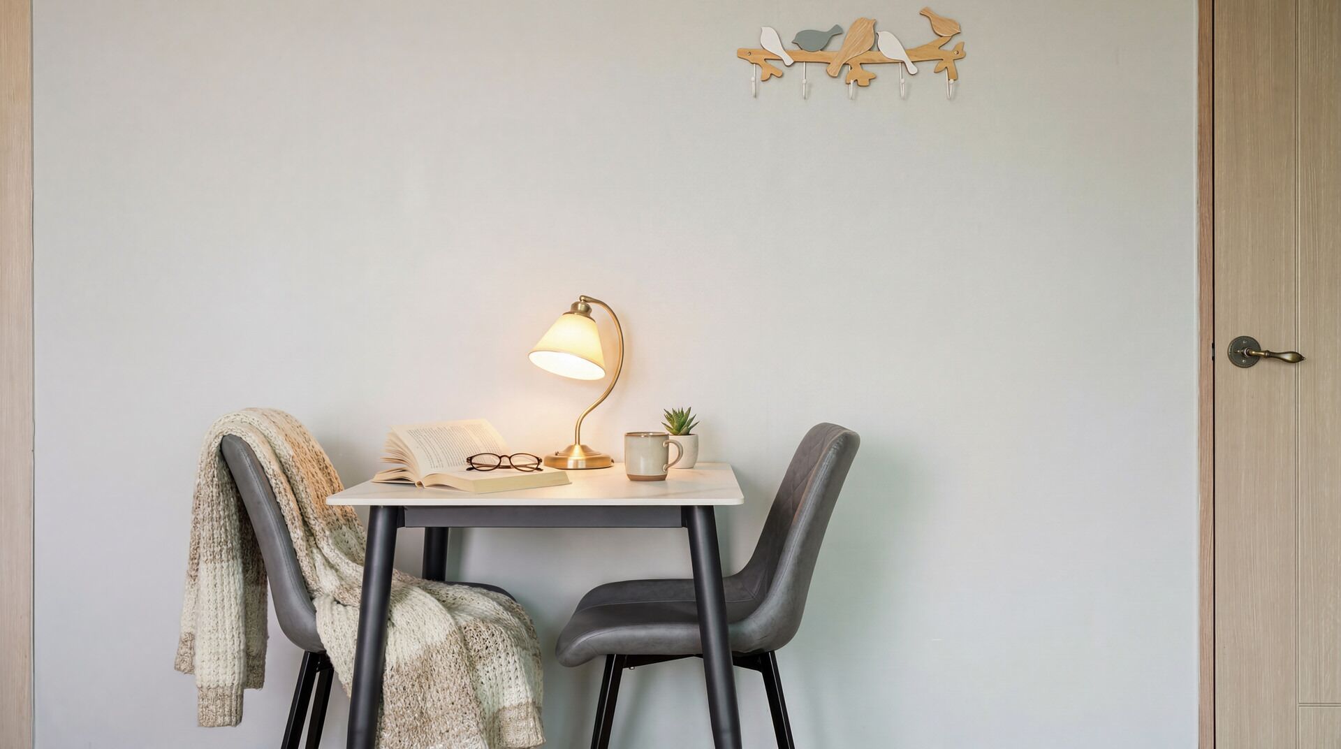 A study area with a desk, chair, lamp, book, glasses, mug, and a small plant.