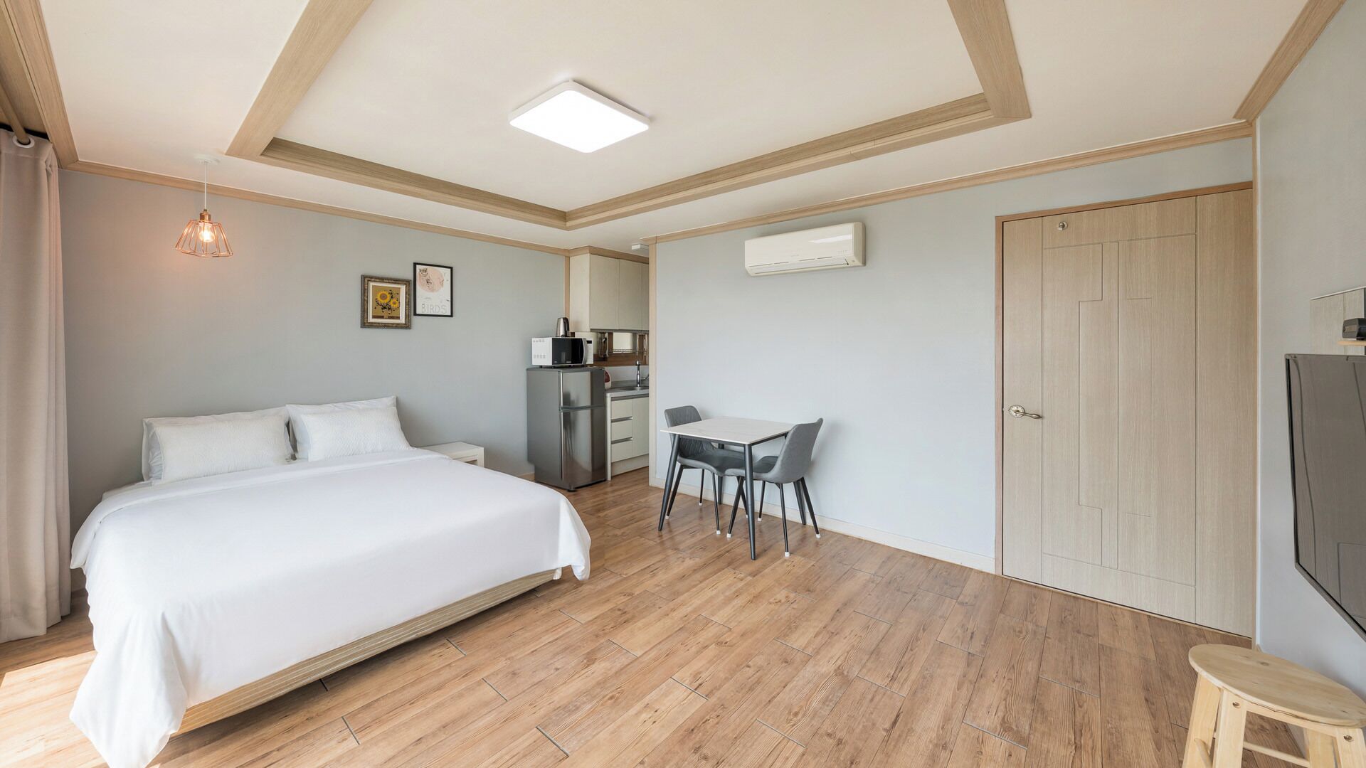A bedroom with a bed, a desk, a chair, a wardrobe, and an air conditioning unit.