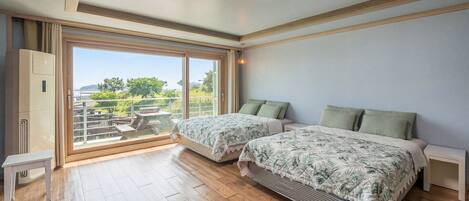 A bedroom with two beds, a sliding glass door to a balcony, and a view of greenery.