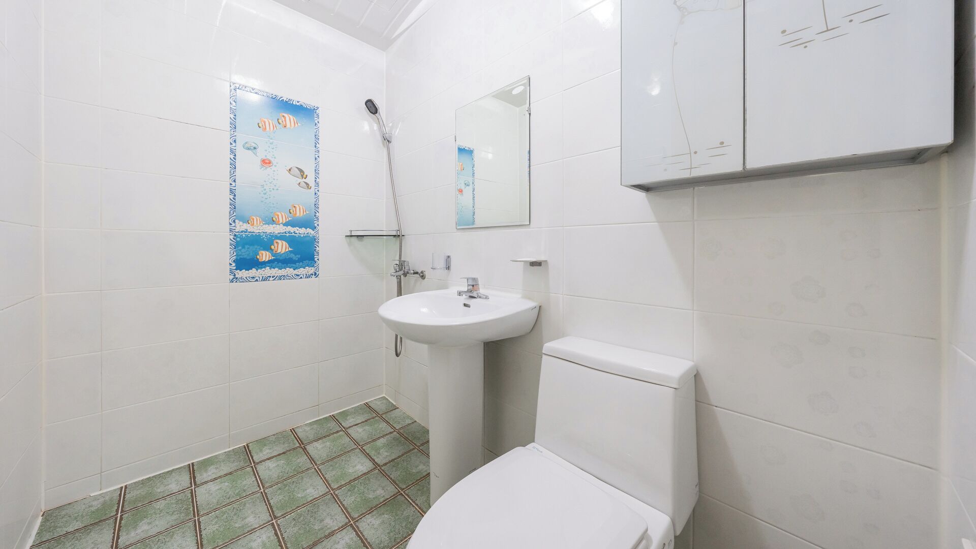 A bathroom with a white sink, toilet, and shower. There is a poster with fish on the wall.
