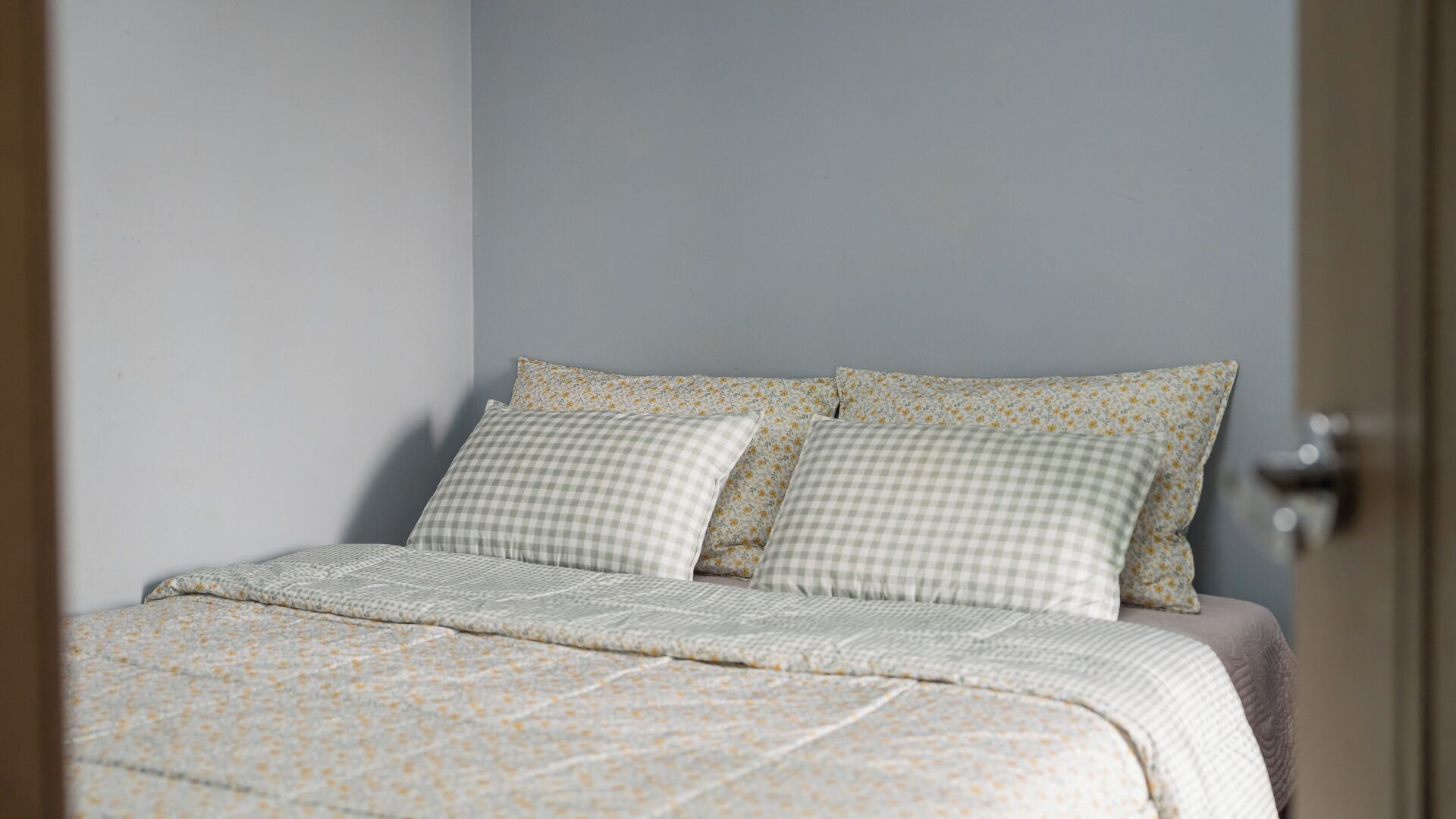 Een bed met een geruit kussen en een bloemenbedekte sprei.