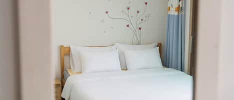 Una cama bien hecha con sábanas blancas, cabecera de madera y decoración de pared con un árbol y corazones.