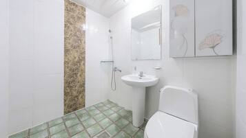 Un baño con azulejos blancos, una zona de ducha con azulejos verdes, un lavamanos blanco y un inodoro.