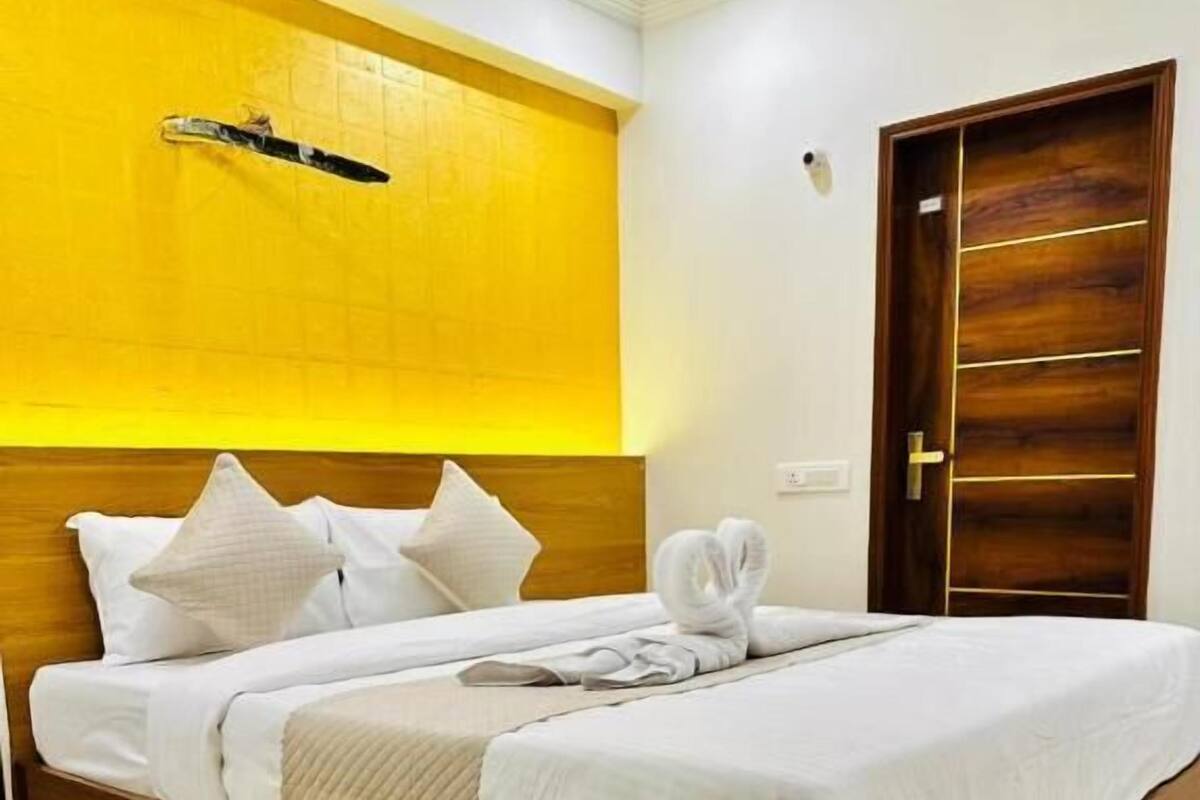 Habitació d'hotel amb un llit de fusta, roba de llit blanca, una paret d'accent groga i una porta de fusta.
