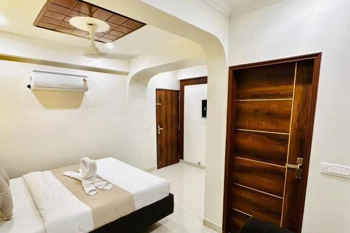 Habitació d'hotel amb llit, porta de fusta, ventilador de sostre i aire condicionat fixat a la paret.
