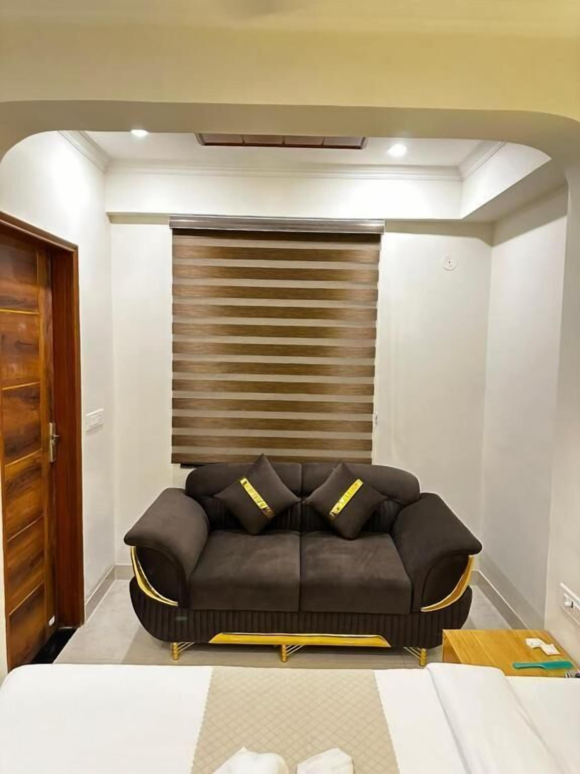 A room with a sofa, a window with blinds, a door, and a ceiling light fixture.