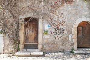 A stone building with two wooden doors, a stone wall with a floral mural, and a small stone step leading to the entrance.