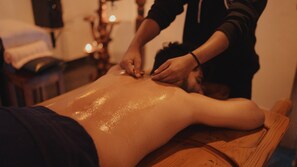 A massage therapy session in progress with a wooden table and a person lying face down. - Ecstacy (Shoolagiri)