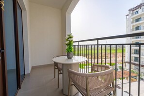 Ein Balkon mit rundem Tisch, zwei Korbstühlen, einem Blumentopf und Blick auf eine Wohngegend.