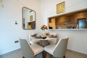 Un coin repas avec une table ronde, quatre chaises, un vase avec des fleurs, un miroir et un comptoir de cuisine doté de placards et d’un réfrigérateur.