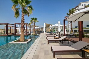Ein Poolbereich mit Liegestühlen, Palmen und Sonnenschirmen.