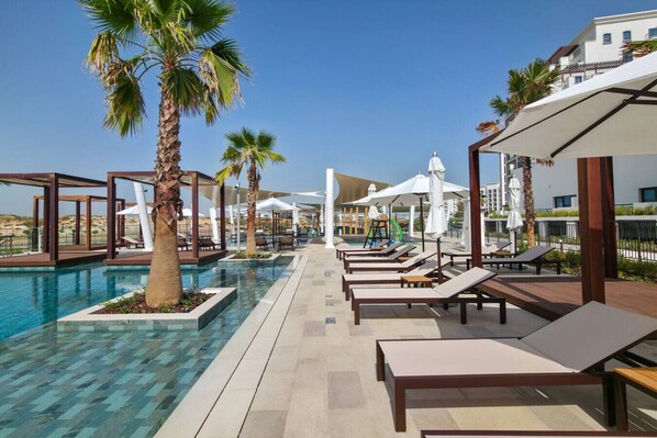 Un espace piscine avec des chaises longues, des palmiers et un ciel dégagé.