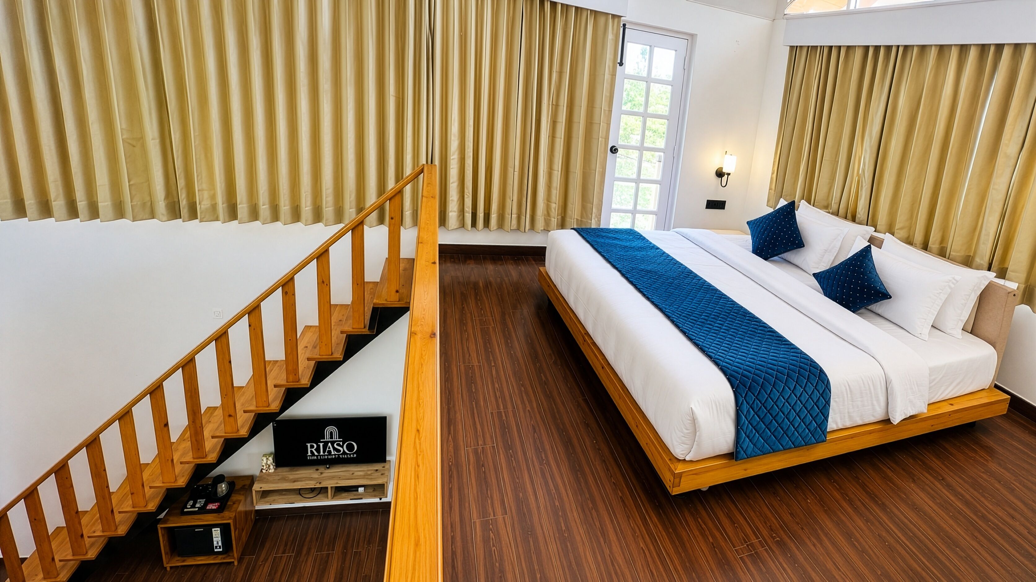 A bedroom with a wooden staircase, a bed with white and blue bedding, and a window with curtains.