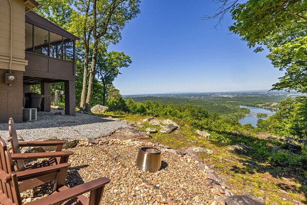 A modern building with a patio area, a fire pit, and a view of a river and forest.