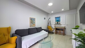 Ein Wohnzimmer mit einer Couch, einem Glastisch, einem Hänge-Sessel, einem Esstisch und einer Topfpflanze.