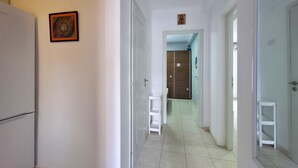 Ein Flur mit einem weißen Kühlschrank, einer Tür mit einer Blumendekoration und einem kleinen weißen Hocker.