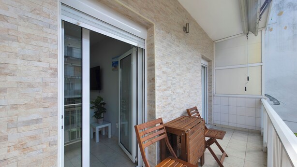 Ein Balkon mit Holztisch und -stühlen, einer Schiebeglastür und einem Blumentopf.