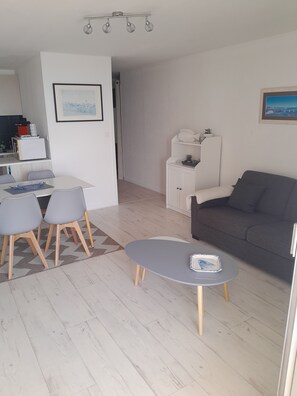 A modern living room with a grey sofa, a small round table, and a dining area with a white table and grey chairs. - Studio Remblai Sables d'Olonne facing the sea (sleeps 3 to 4) (Les Sables-d'Olonne)