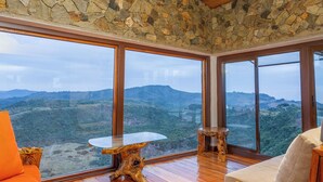 Una habitación con paredes de piedra, ventanas amplias, suelo de madera y vistas a un paisaje montañoso.