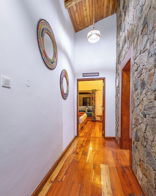 Un pasillo con suelo de madera, pared de piedra y una puerta que da a una habitación con cama y ventana.