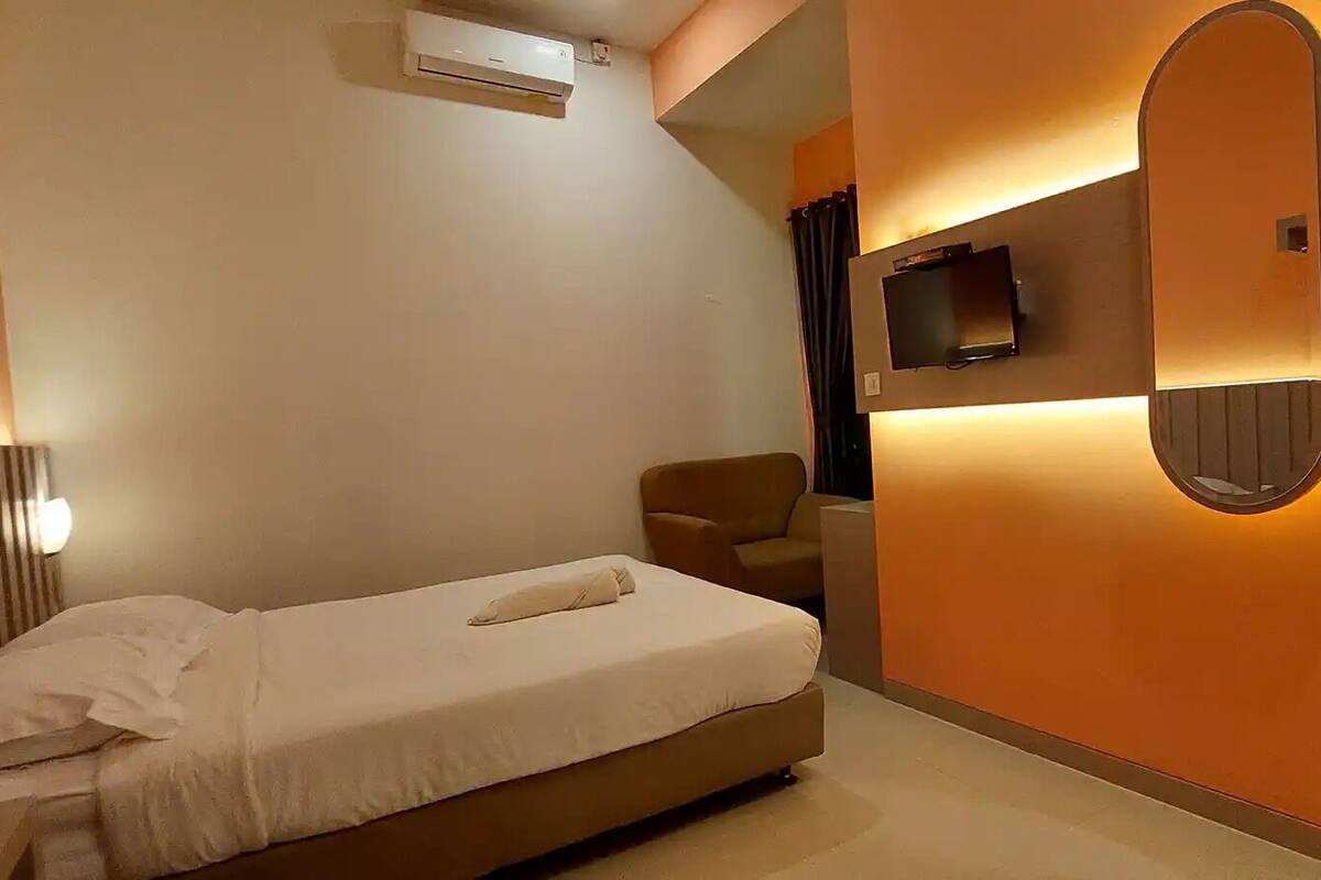 Una habitación de hotel moderna con cama, una silla, un televisor de pantalla plana y un equipo de aire acondicionado.