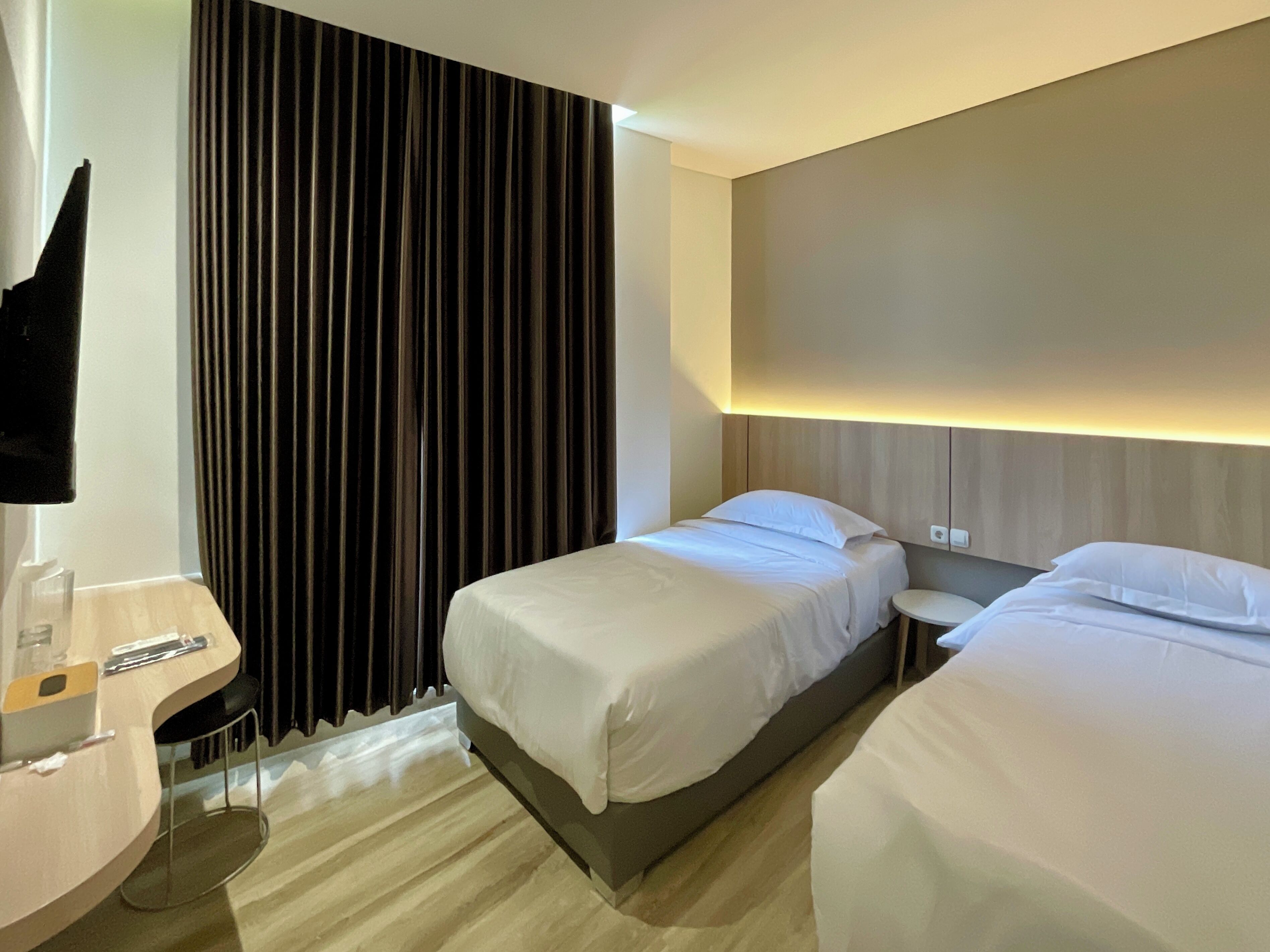 Hotellihuone, jossa on kaksi sänkyä, yöpöytä, lamppu ja suuri ikkuna, jossa on verhot.