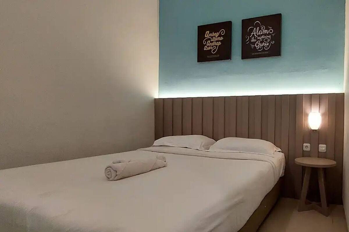 Una habitación de hotel con una cama, una mesita redonda pequeña y dos lámparas fijadas a la pared.