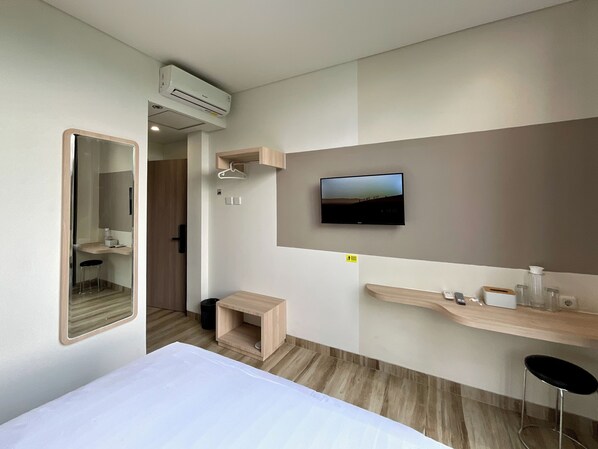 A modern hotel room with a bed, a TV mounted on the wall, a small wooden stool, and a mirror. - Oemah Djari Hotel Syariah (Salatiga)